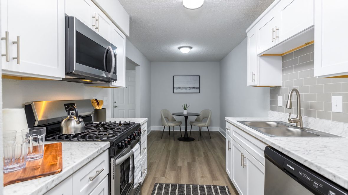 An exquisite, renovated galley-style kitchen boasting Carrara countertops, white shaker cabinets, stainless-steel appliances, and a modern grey subway tile backsplash, creating a stylish and functional culinary space.