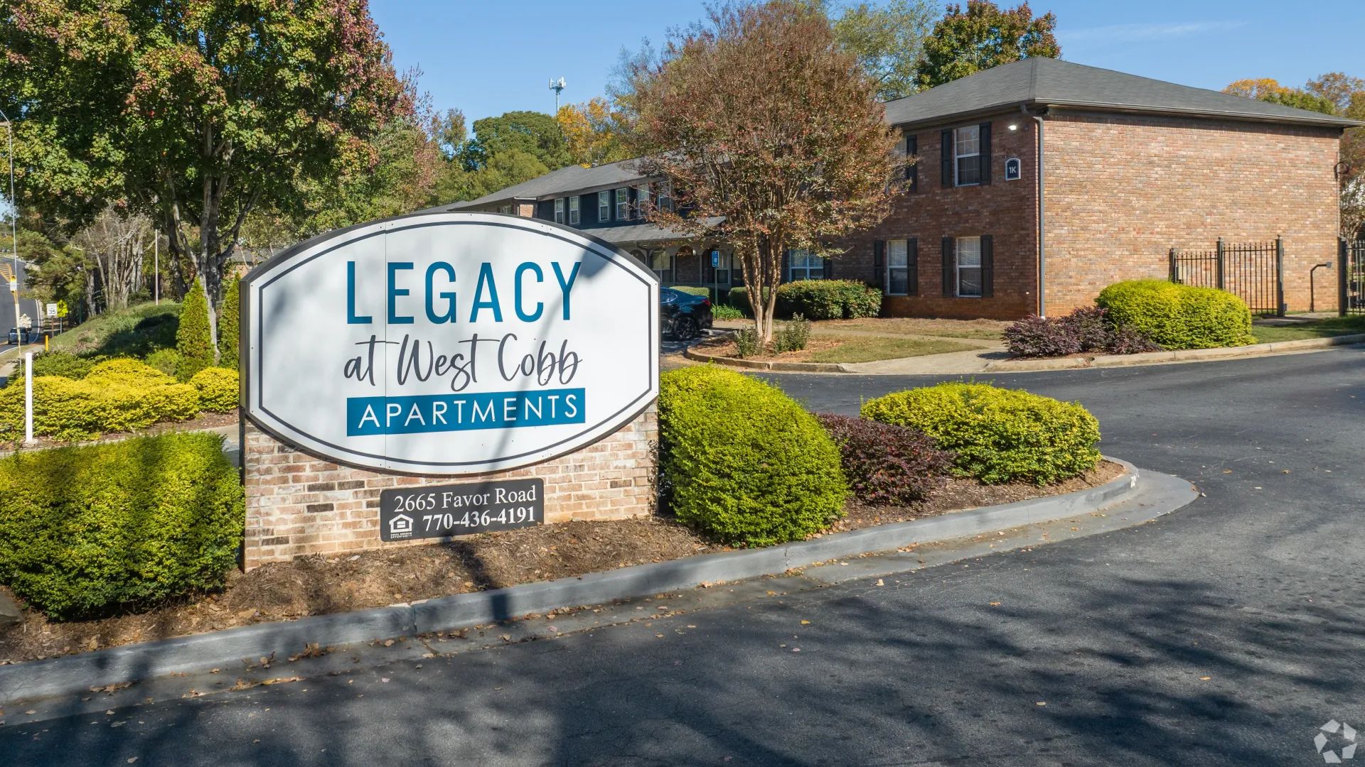 Entrance sign for Legacy at West Cobb Apartments in Marietta, GA, surrounded by landscaped greenery and trees.