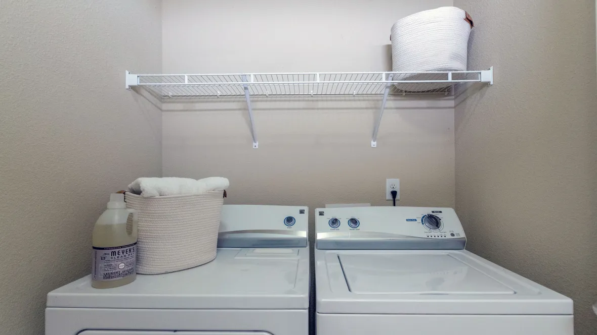 A full-size washer and dryer set complete with open wire shelving above appliances for convenient storage in all homes.
