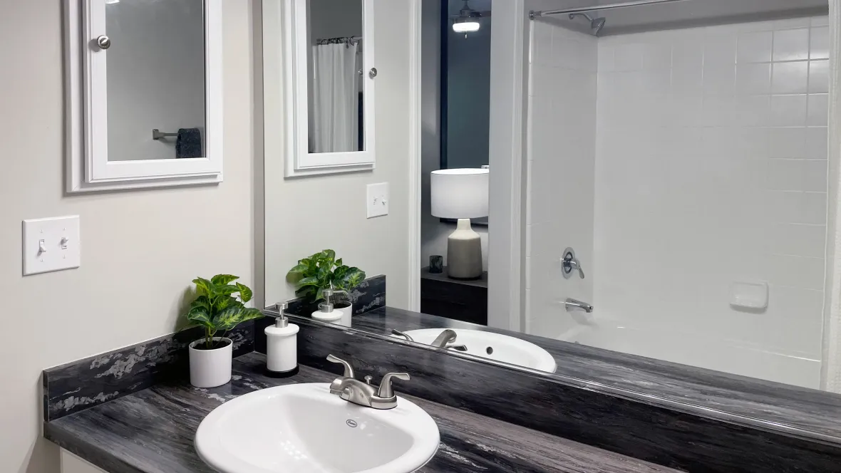 Extended bathroom mirror with peek of black fusion countertops, modern medicine cabinet, and vanity lighting.