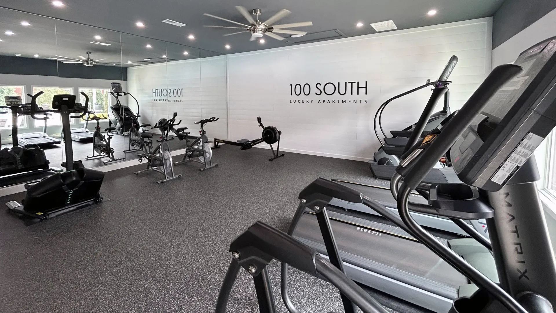 Fitness studio at 100 South Luxury Apartments featuring mirrored walls, cardio equipment, and a variety of machines in a bright, modern space.