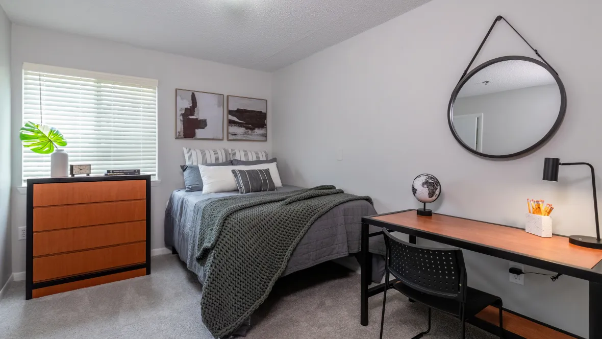 An inviting bedroom with plush carpeting, generously-sized windows adorned with wood-style privacy blinds, and ample overhead lighting.