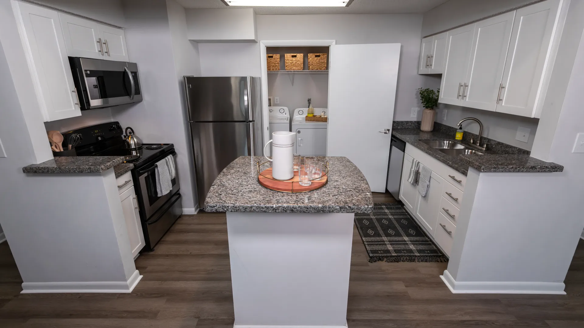 Modern kitchen with granite-style countertops, stainless steel appliances, white cabinetry, an island, and a built-in pantry with wicker baskets.