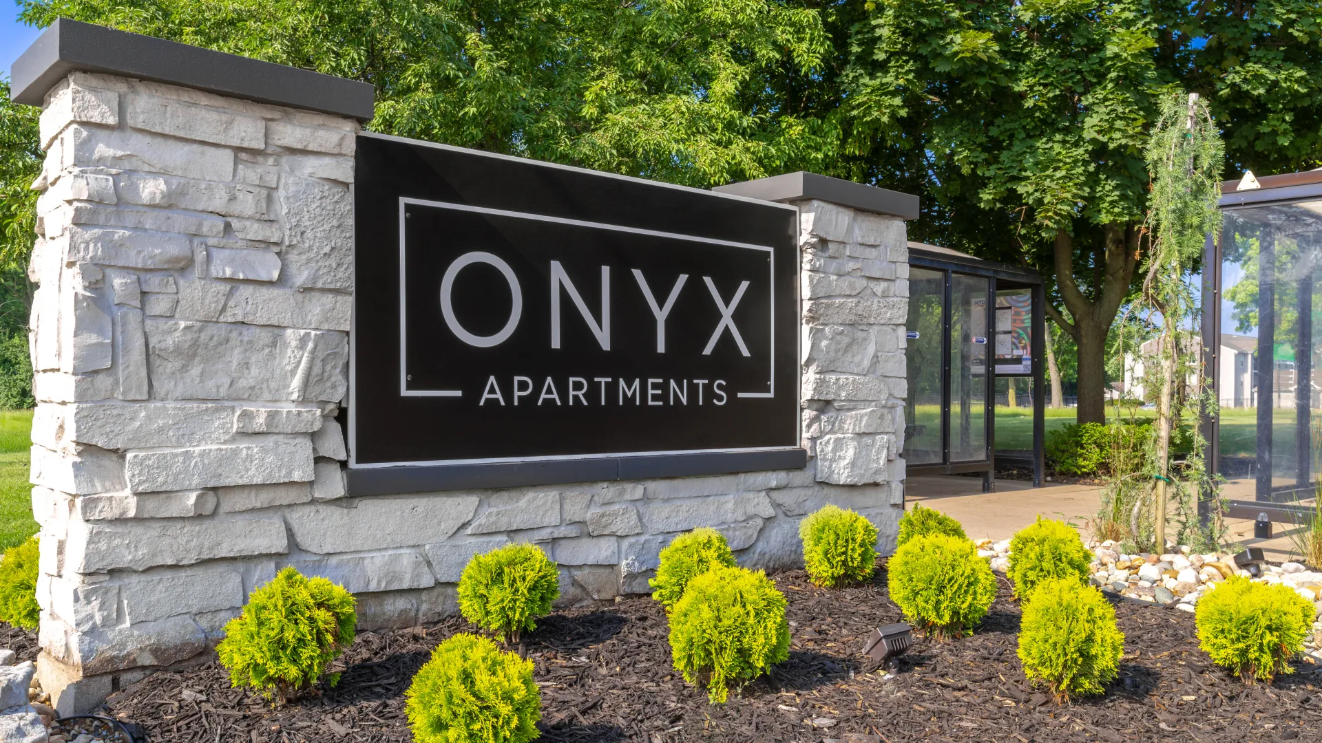 Entrance sign for Onyx Apartments surrounded by lush landscaping and greenery.