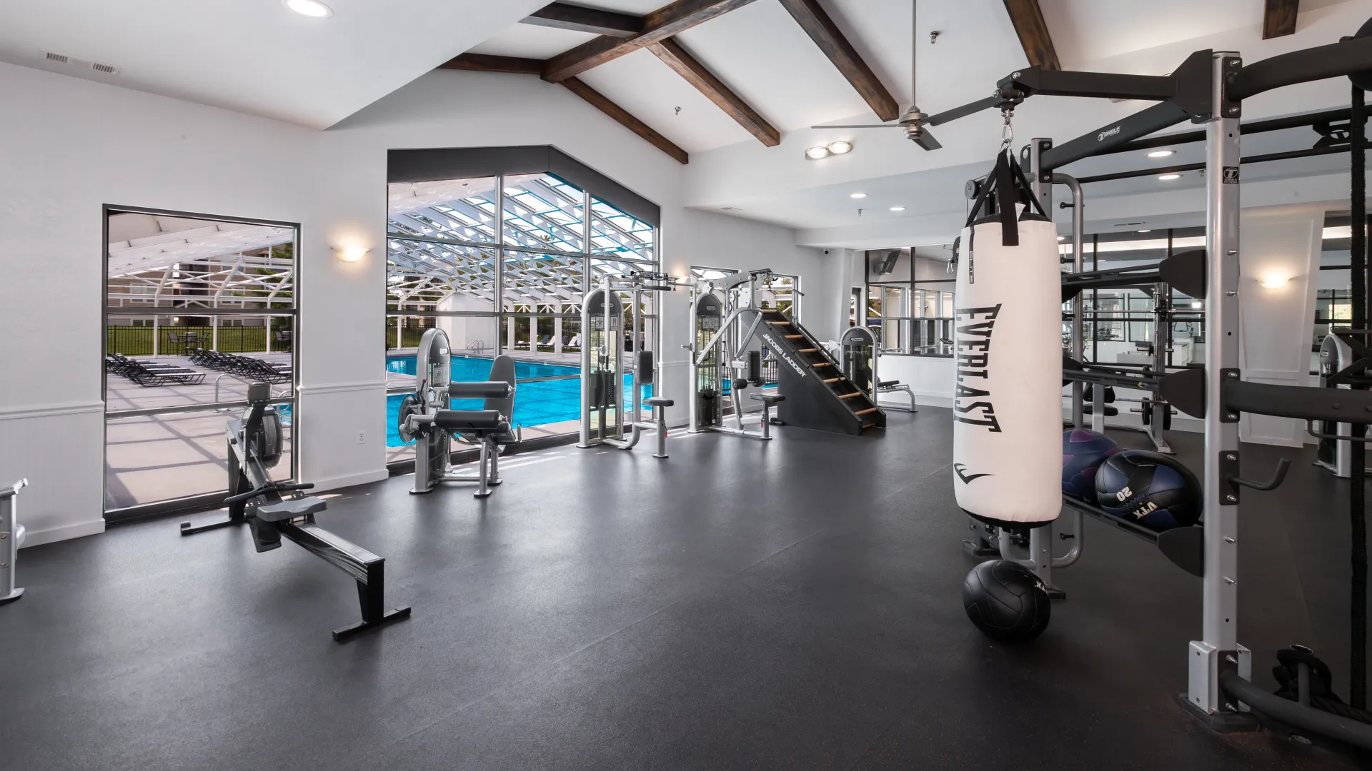 Fitness center featuring a variety of workout equipment, including a punching bag, weight machines, and cardio machines, with large windows offering a view of the indoor pool.