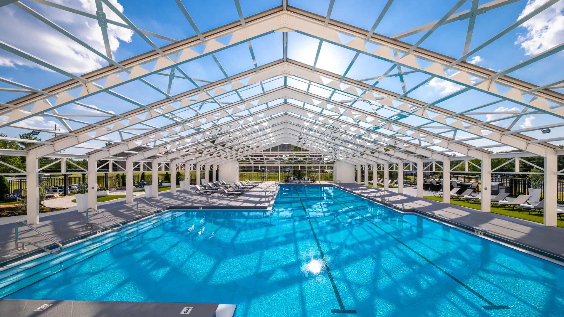 Enclosed pool area with a spacious swimming pool, lounge chairs, and natural light streaming through the glass roof structure.