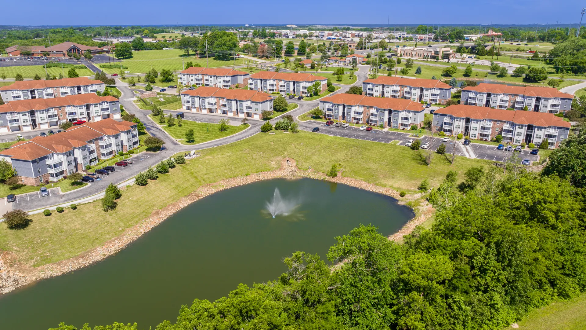 Aerial view of Lenox West showing multiple residential buildings, a central pond with a fountain, and surrounding greenery.