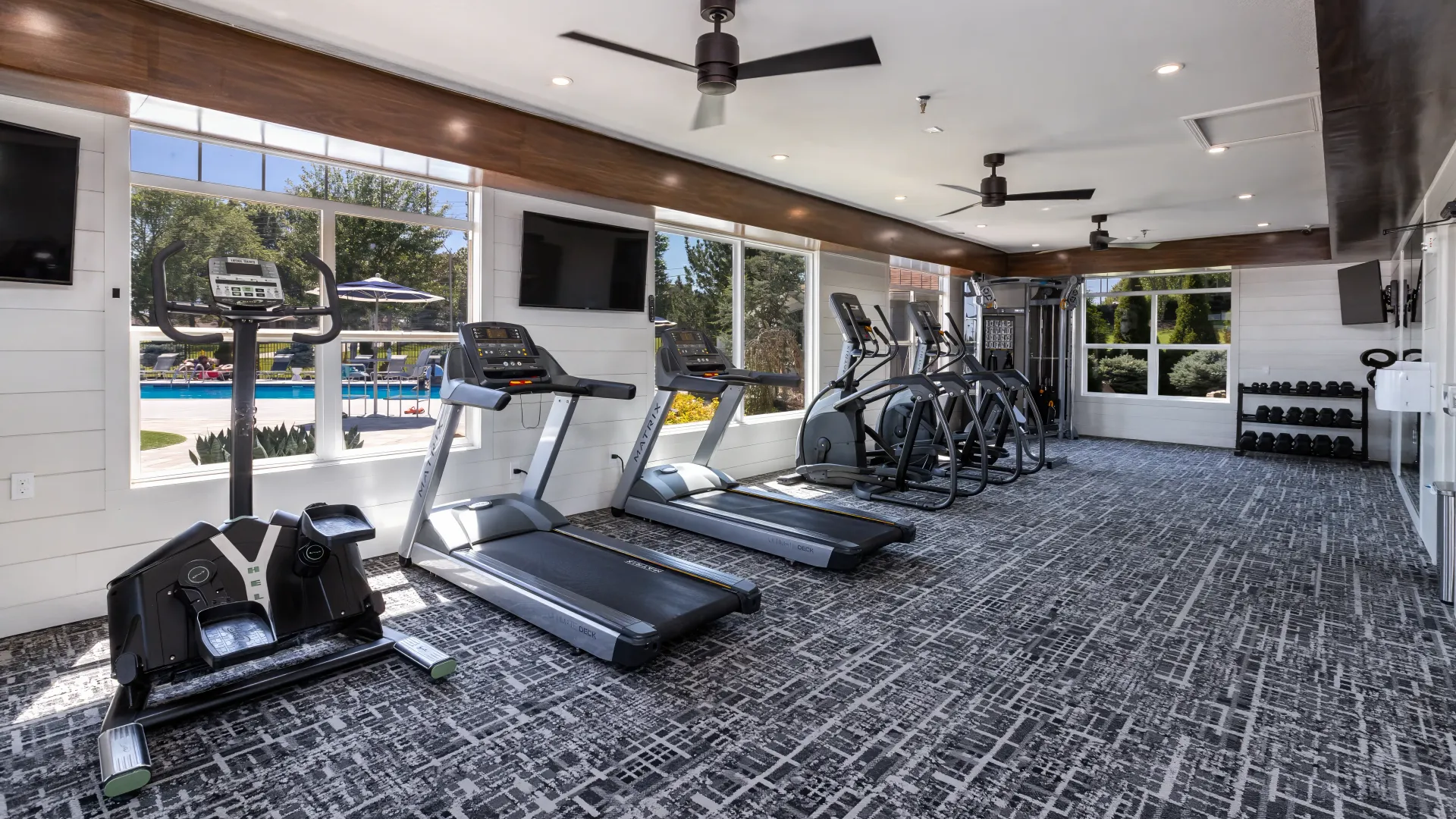 Interior of a fitness center at Lenox West featuring treadmills, ellipticals, and a pool view through large windows.