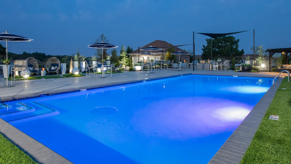 An expansive, illuminated pool deck at night with glowing pool waters