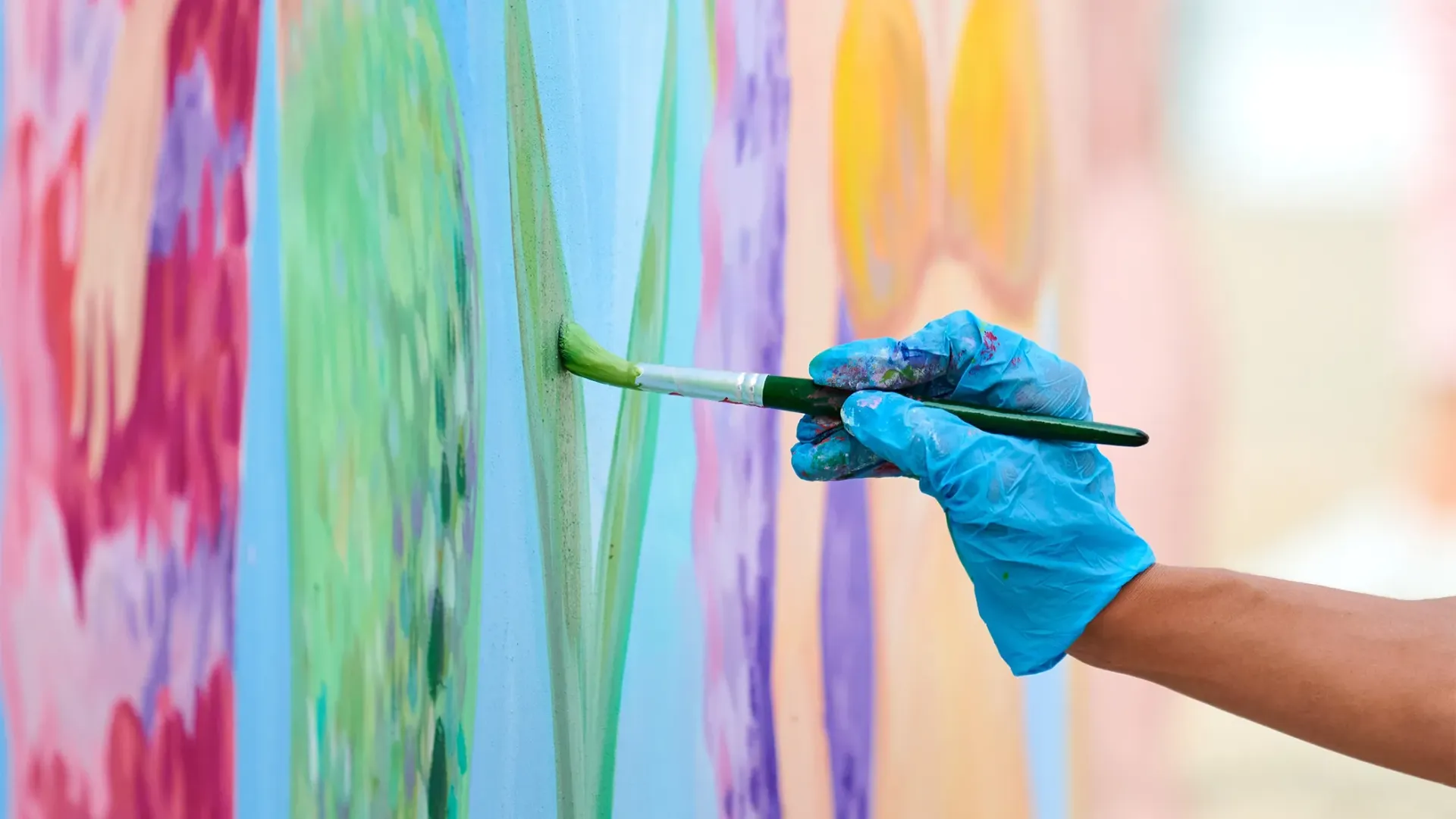 A hand holding a paint brush to a wall, painting a wall art mural