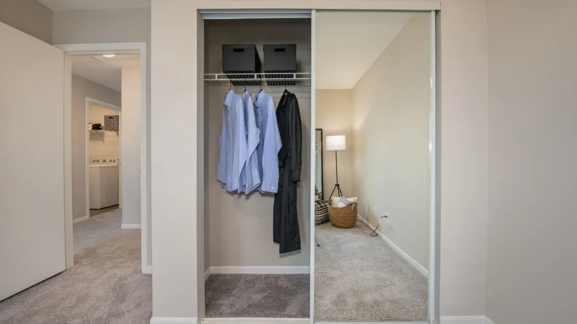 A bedroom closet with ample space, open wire shelving, and sliding mirror doors.