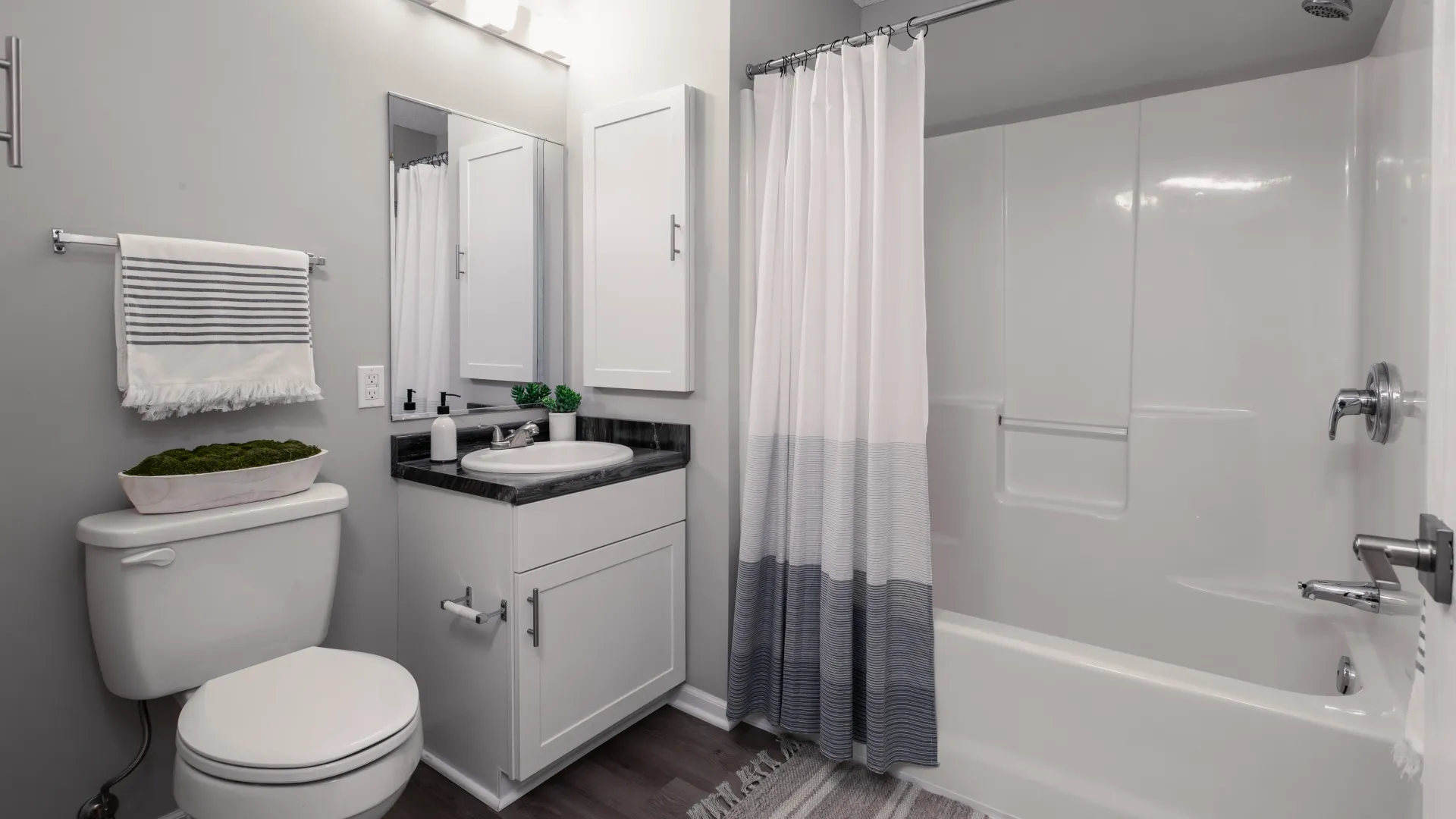 Modern bathroom with a white vanity, gray countertop, white toilet, striped towel, and a shower with a white curtain.