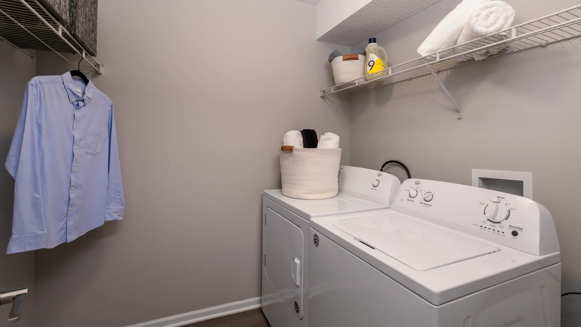A laundry room with a washer, dryer, and shelving for storage and hanging clothes.