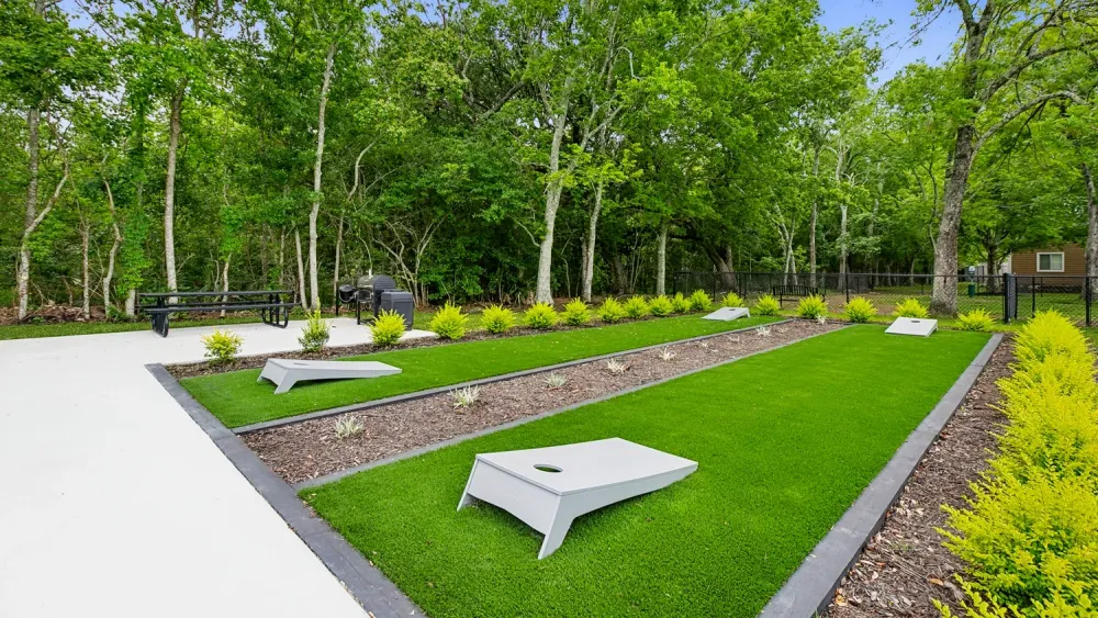 Cornhole boards on lush, green grass surrounded by trees