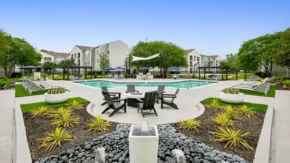 A fire pit surrounded by Adirondack chairs on a lushly landscaped pool deck