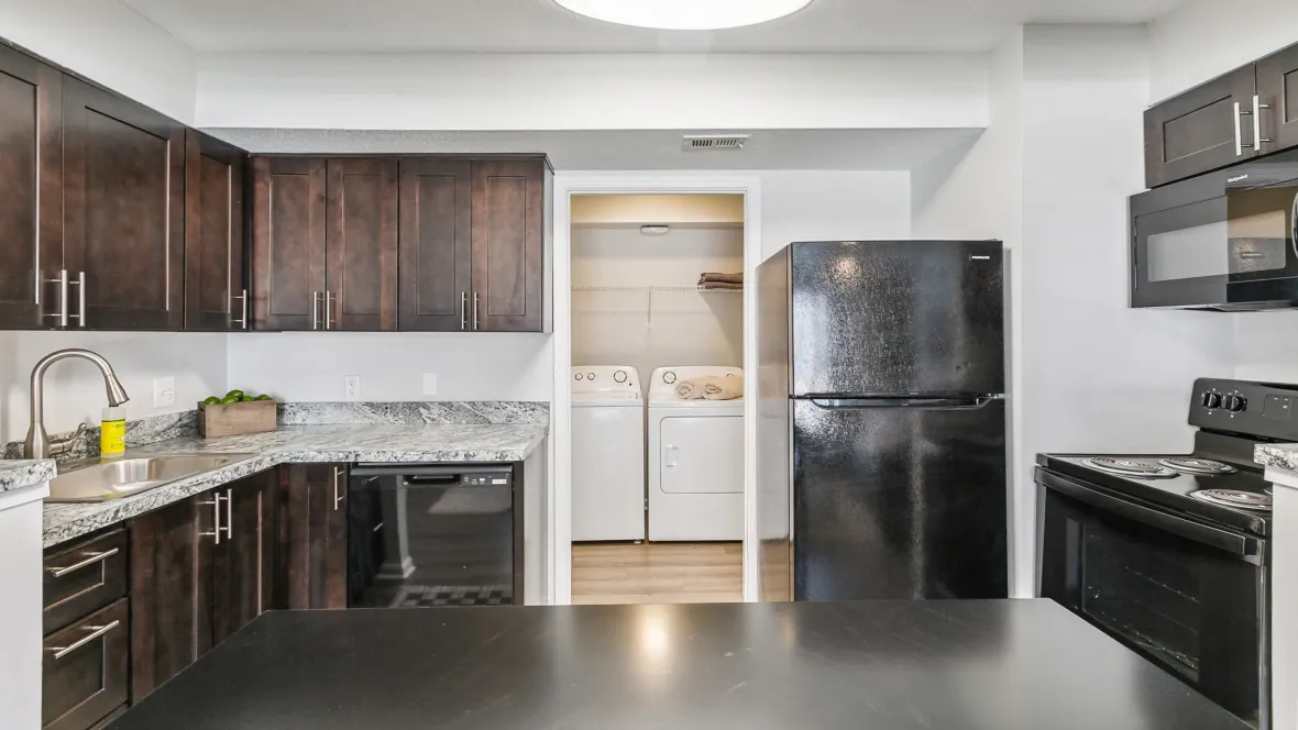 A well-appointed kitchen area, adorned with a sleek black appliance package, a sneak peek into the convenient adjacent laundry room, and chic espresso cabinetry.
