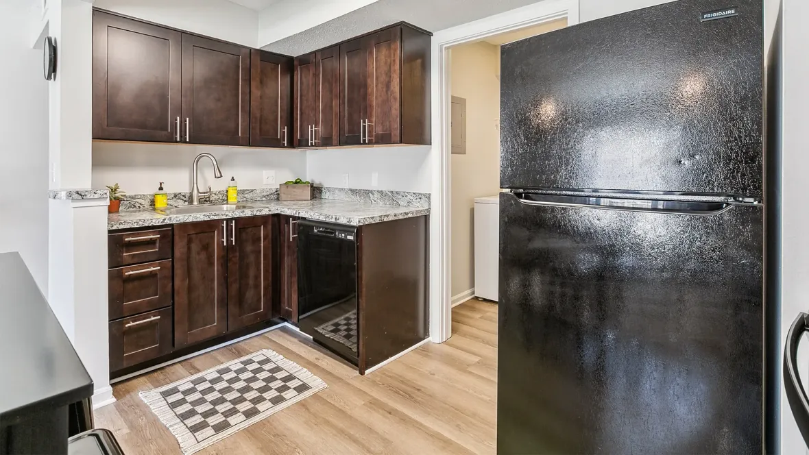 A view of sleek dark brown cabinets with contemporary brushed nickel accented handles and a goose neck faucet with gorgeous light brown wood-like floors – creating a perfect canvas for culinary creativity. 