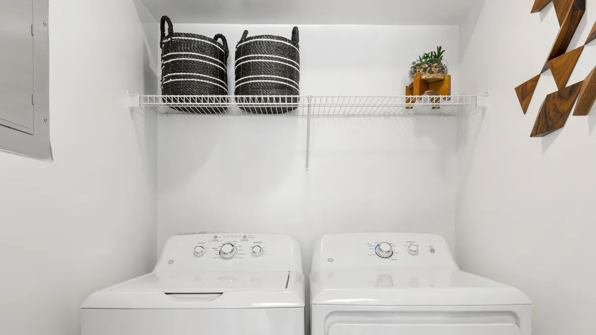 A convenient in-unit laundry setup with open wire shelving above the washer and dryer.