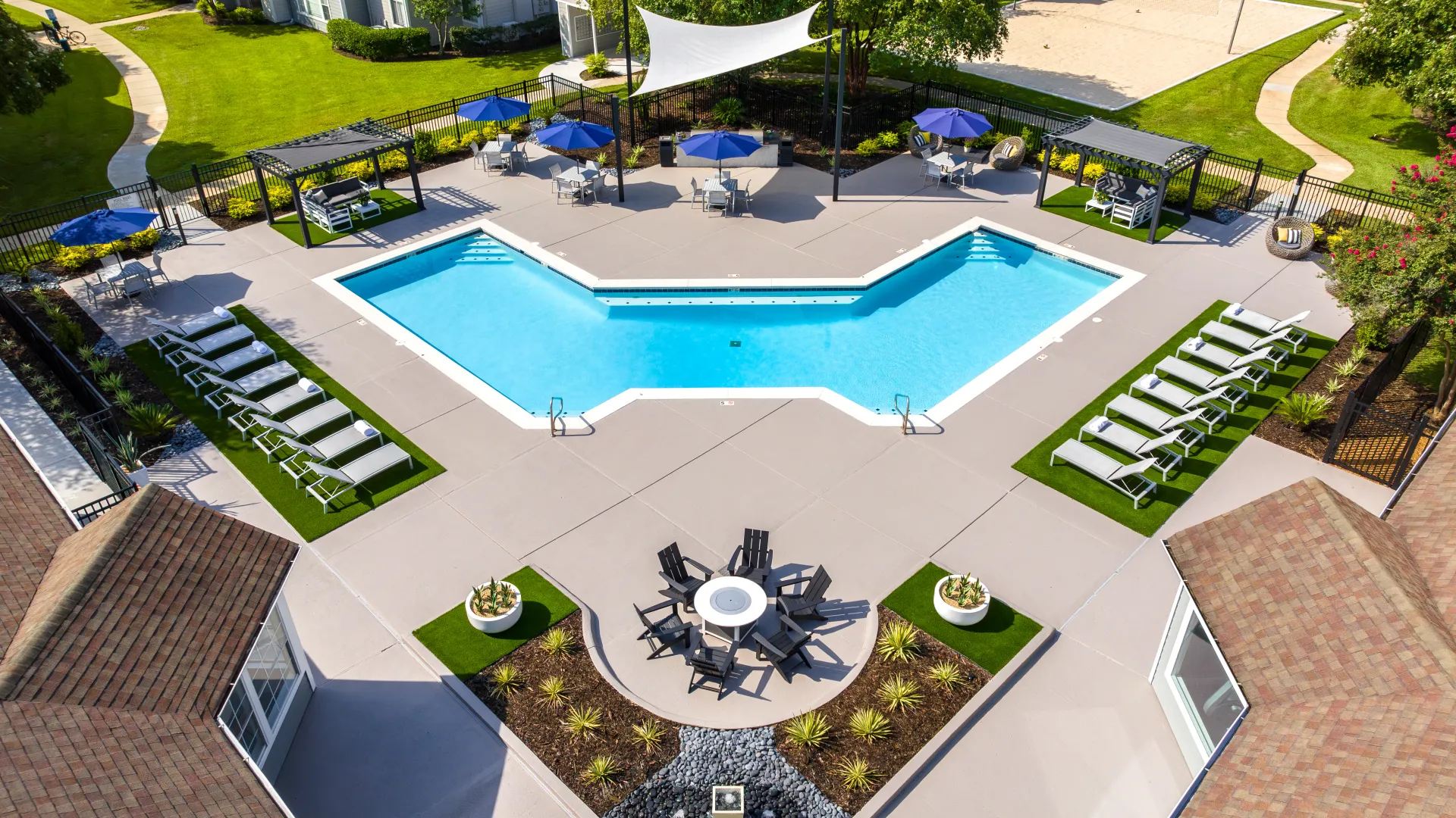 Aerial view of the pool area at Maison Burbank, featuring lounge chairs, shaded seating, a fire pit, and surrounding green lawns.