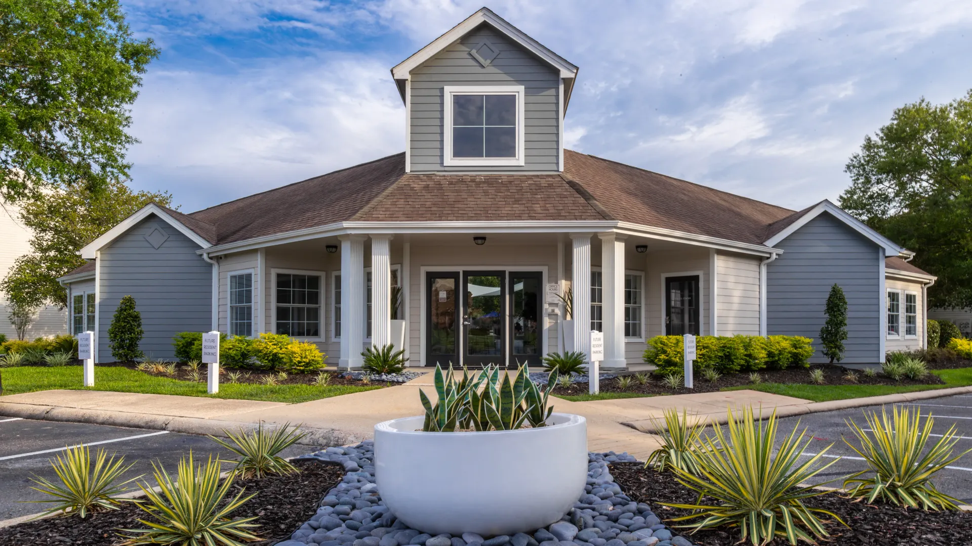 Exterior view of the Maison Burbank office building, featuring a modern design with grey siding, white pillars, and well-maintained landscaping.