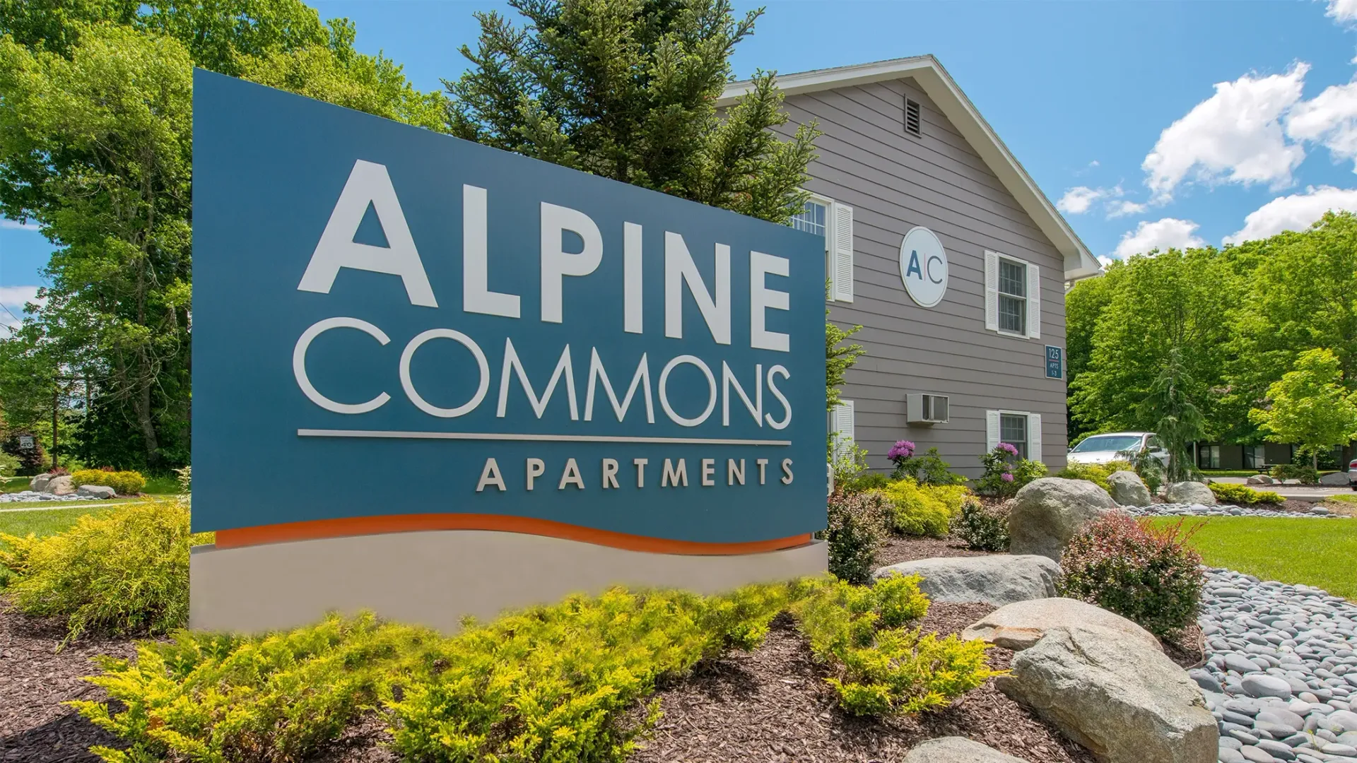 The front sign of the community, reading 'Alpine Commons' surrounded by lush green landscaping