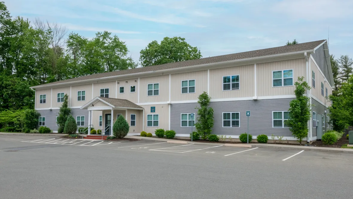 A photo of our apartment building exterior with lush evergreen landscaping and abundant parking spaces, radiating a feel-good vibe.