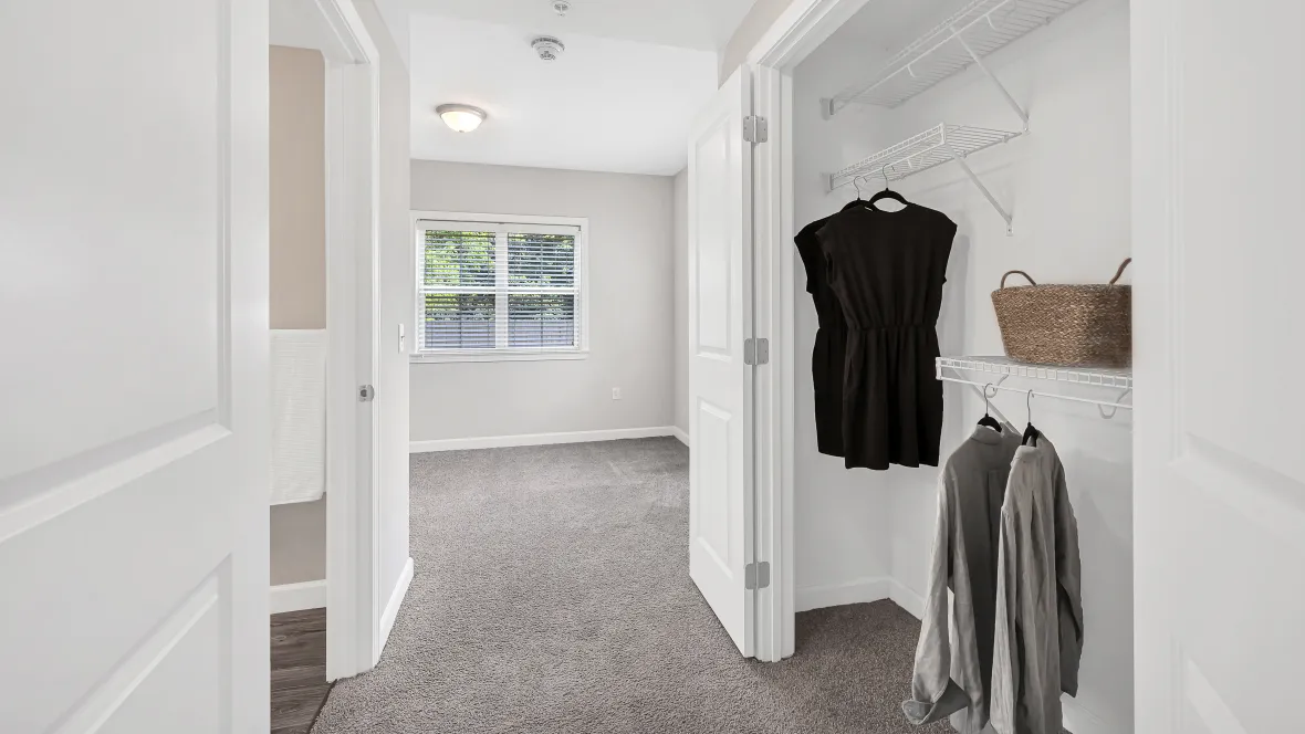 A spacious closet with double doors and open wire shelving organizers located in a hallway between the bedroom and connecting bathroom.