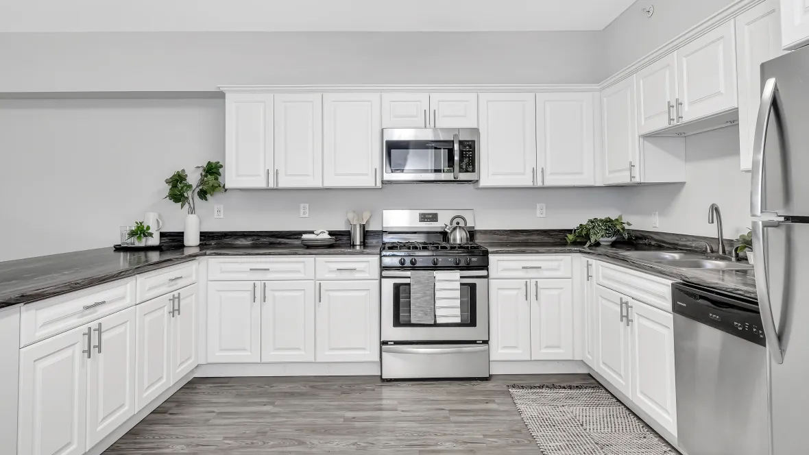 Spacious, well-lit kitchen with white cabinets, stainless steel appliances, wood-style flooring, abundant storage, fridge, stove, dishwasher, microwave, and double sink.