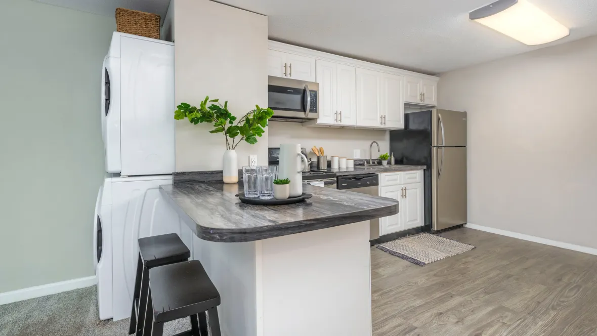Open kitchen featuring white cabinets, stainless steel appliances, breakfast bar, and wood-like flooring, accompanied by a centrally located washer and dryer just left of the breakfast bar.