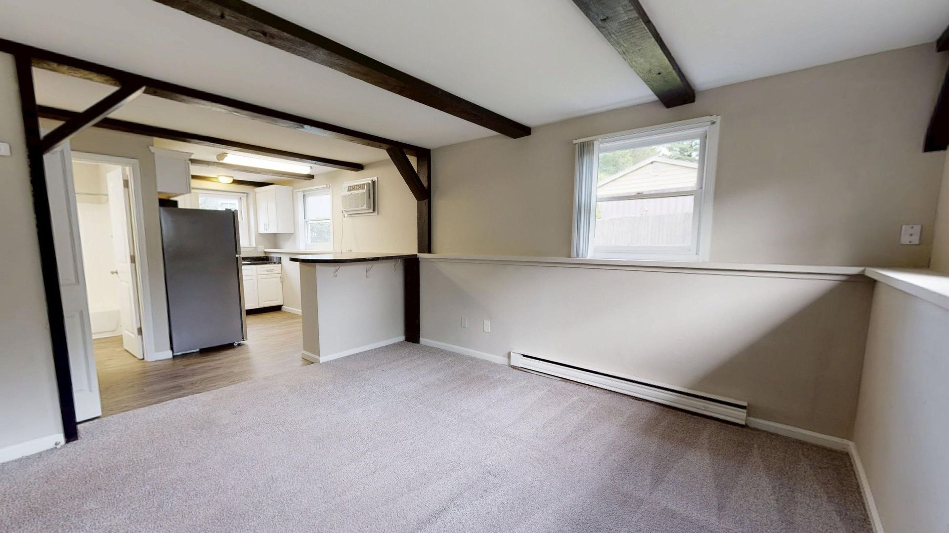 Bright living room in a studio apartment with exposed beams and open kitchen entry.