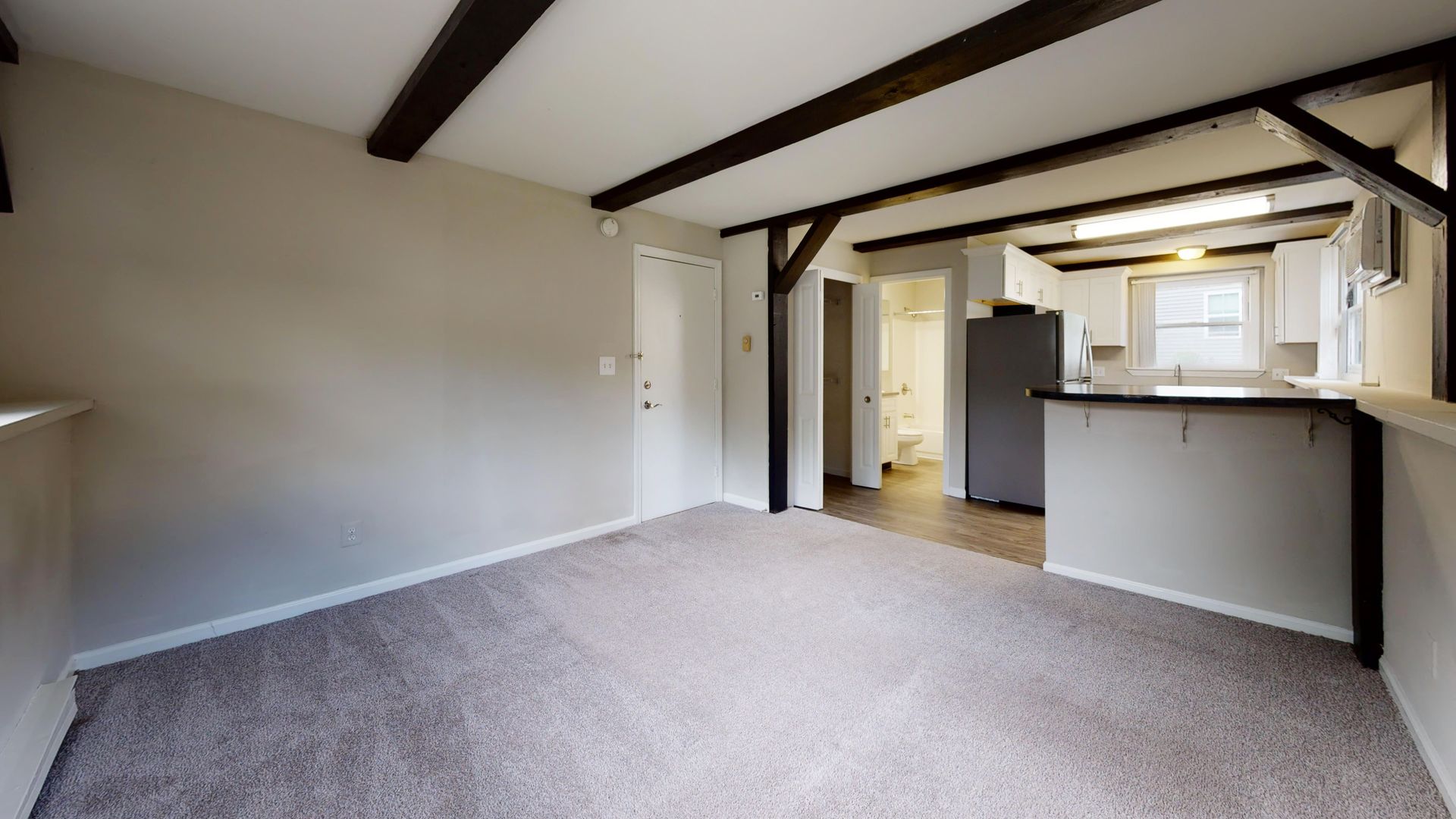 Open floor plan with exposed wood beams and visible kitchen appliances from the living area.