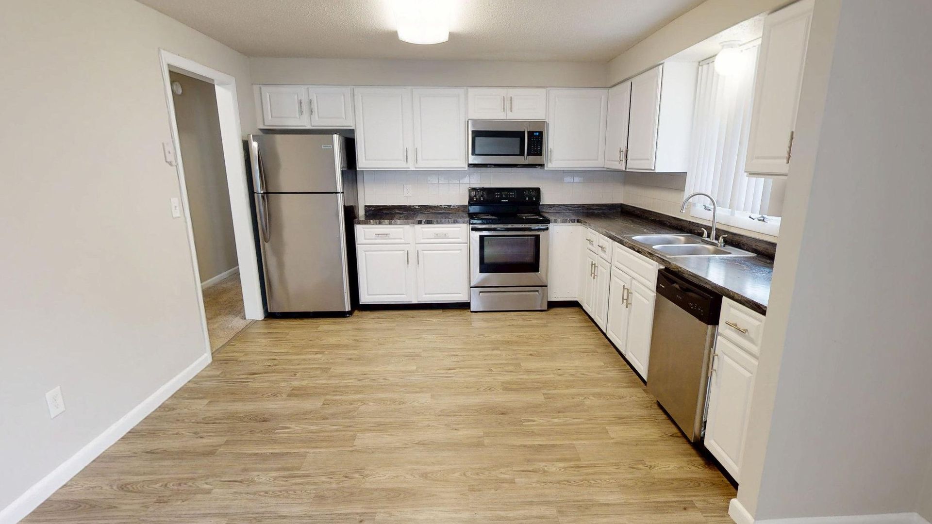 Spacious kitchen with stainless steel appliances, white cabinets, and wood-style flooring in The Pioneer floor plan.