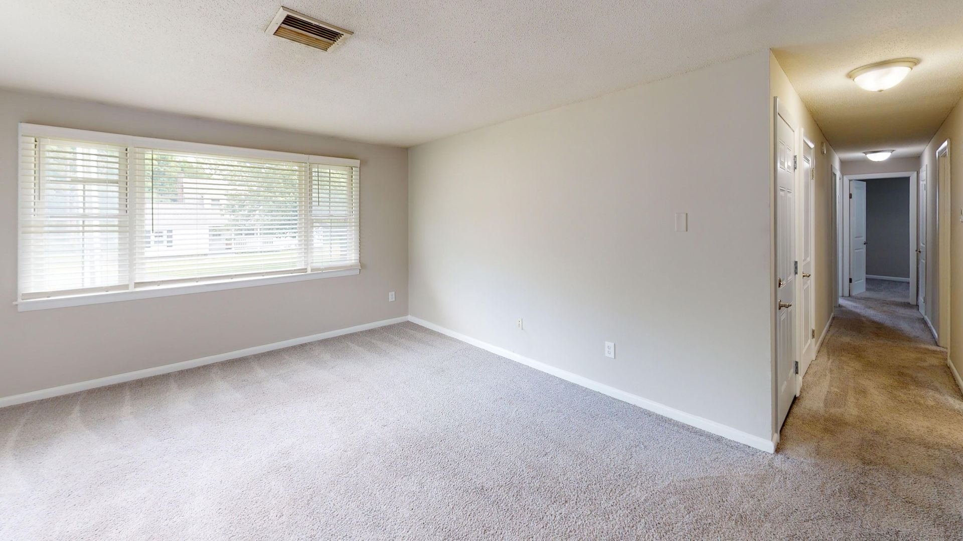Bright living room at Alpine Commons featuring wide windows, light walls, and plush carpeting.