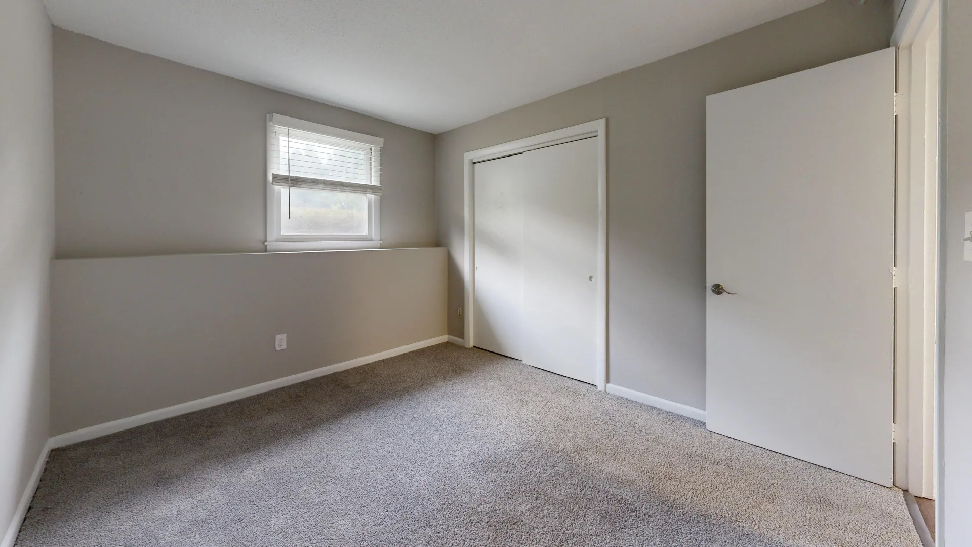 Cozy bedroom in The Valley floor plan at Alpine Commons Apartments with soft carpeting, a large window, and ample closet space.