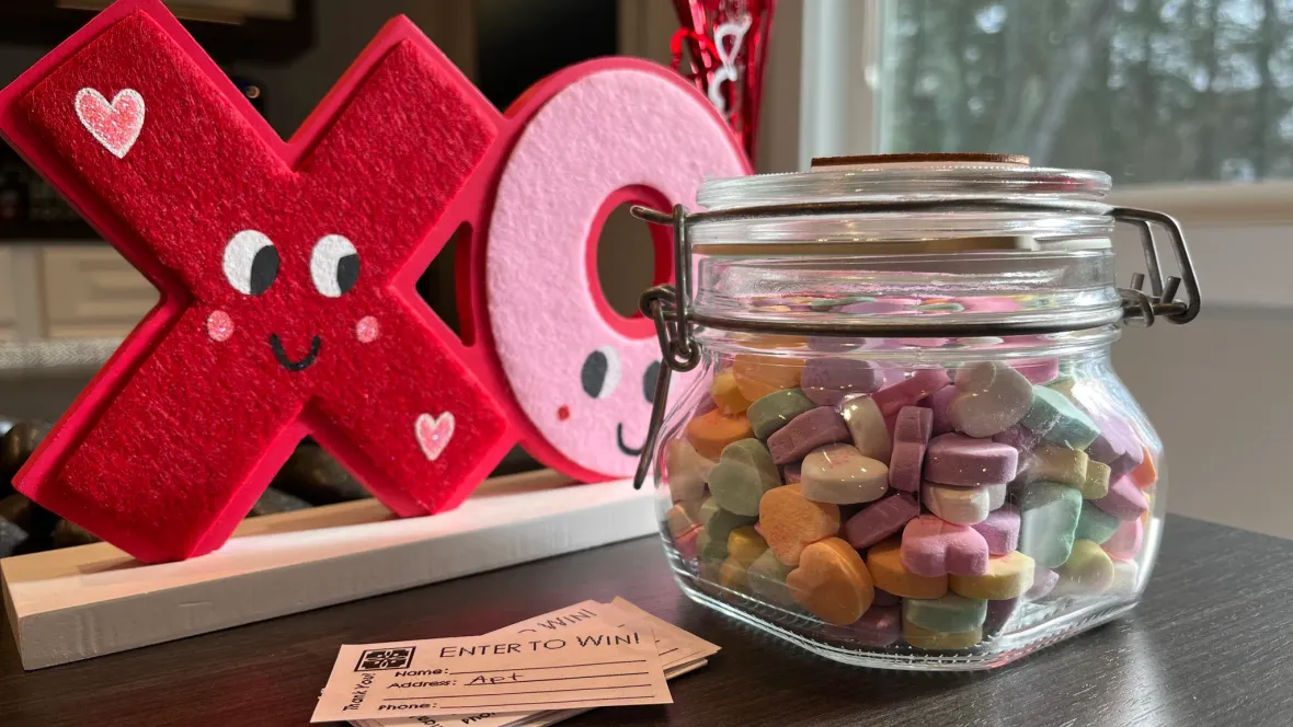 A jar of candy hearts with a cute sign behind that says "XO" with little faces on it.