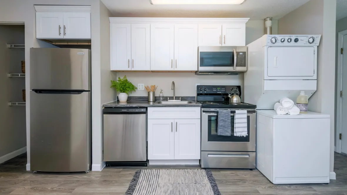 A kitchen with several white upper cabinets. Plus, a walk-in pantry to the left and a stacked washer and dryer to the right of the kitchen.