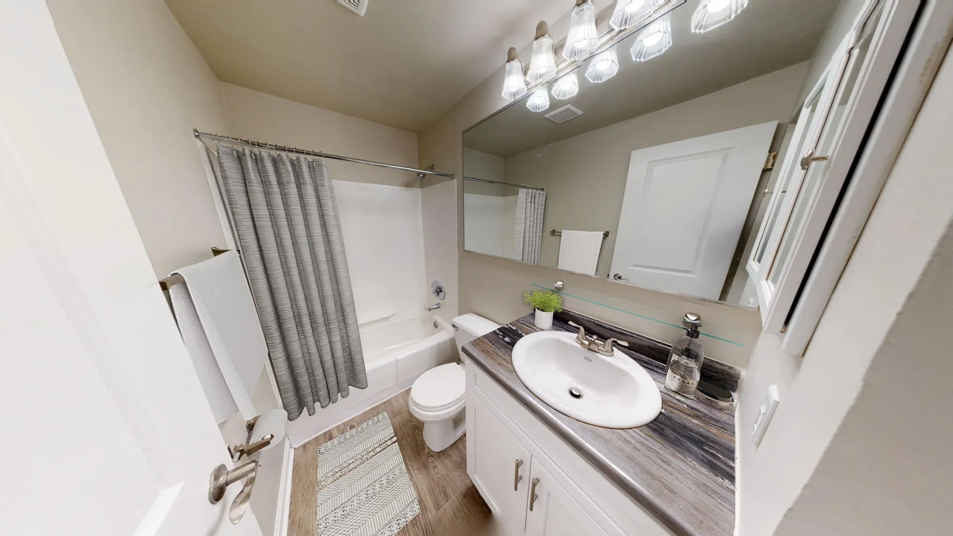 Renovated bathroom in The Dickenson 1 bedroom floor plan at Aspen Chase Apartments featuring a large mirror, upgraded vanity, and wood-style floors.
