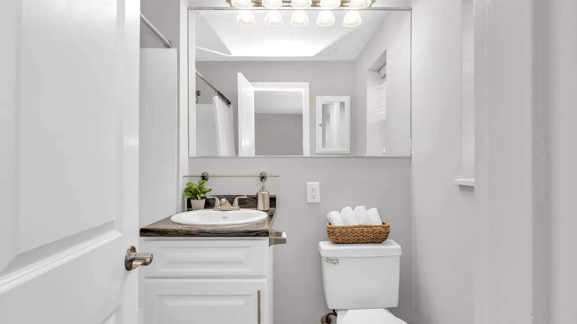 A bathroom featuring an expansive mirror from corner to shower wall, reflecting radiant overhead light.