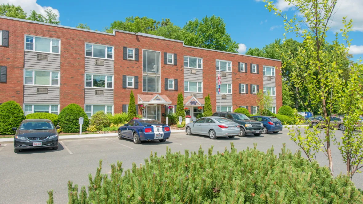 An apartment building with parking spaces in front. There are also some reserved parking signs for those that chose to secure their own parking spaces for an upgrade.