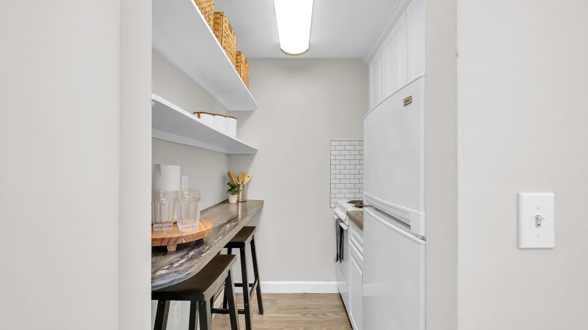 Galley-style kitchen with wall-to-wall counters and shelves on the left and stove, fridge, sink to the right.