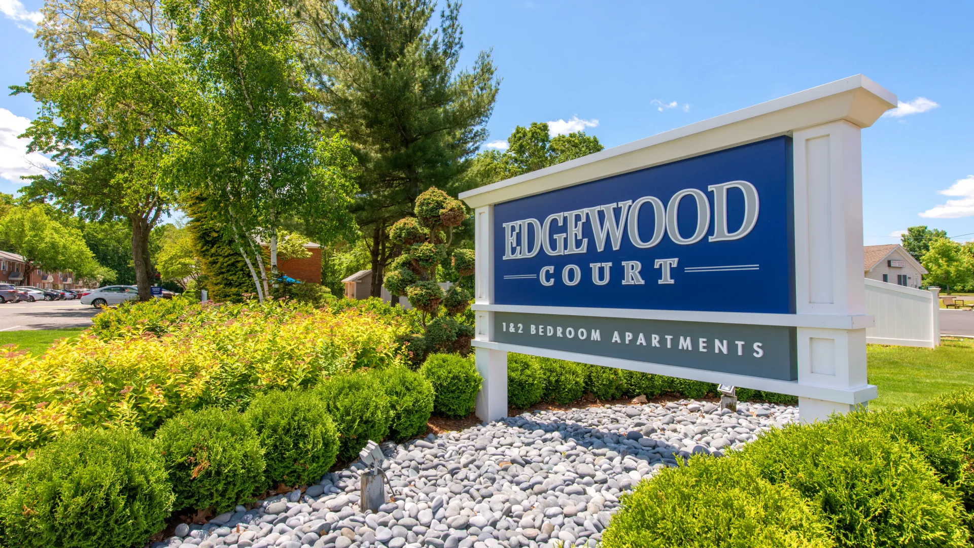 The front sign that reads Edgewood Court, surrounded by lush landscaping, at the front entrance of the apartment community.