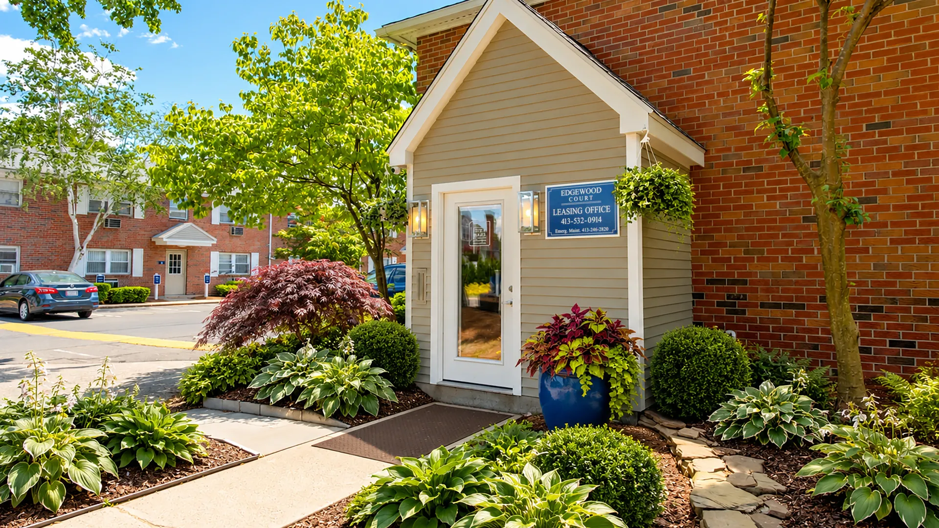 Edgewood Court Apartments leasing office entrance with colorful landscaping, mature trees, and community management office signage.