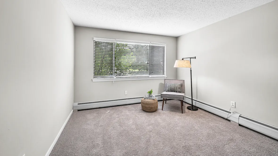 A charming bedroom with plush carpeting, flooded with natural light from a large window, and baseboard floor heaters for the ultimate cozy comfort.