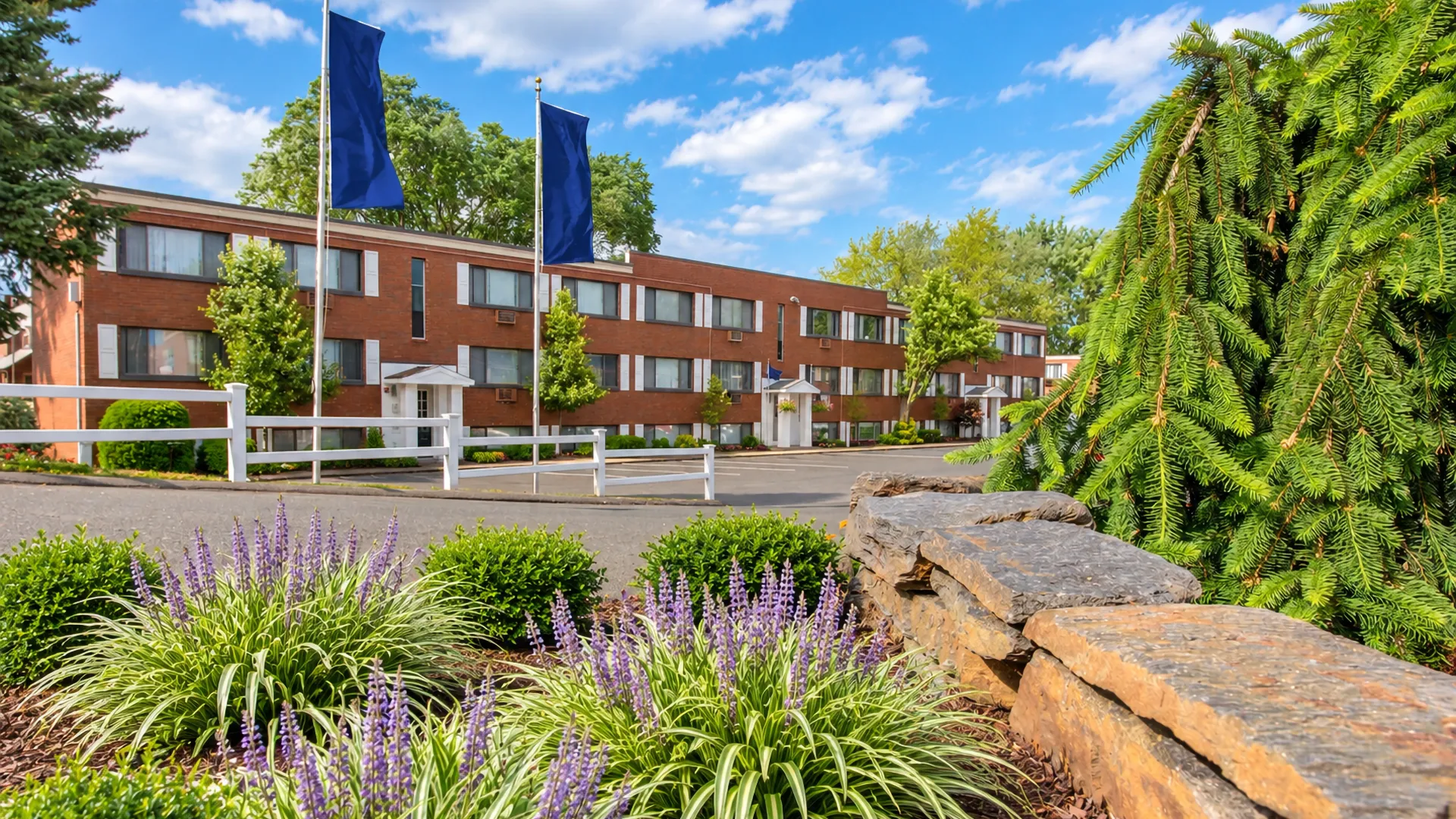 Exterior view of Country Manor's apartment building, flags waving in the breeze, surrounded by meticulously landscaped, welcoming grounds.