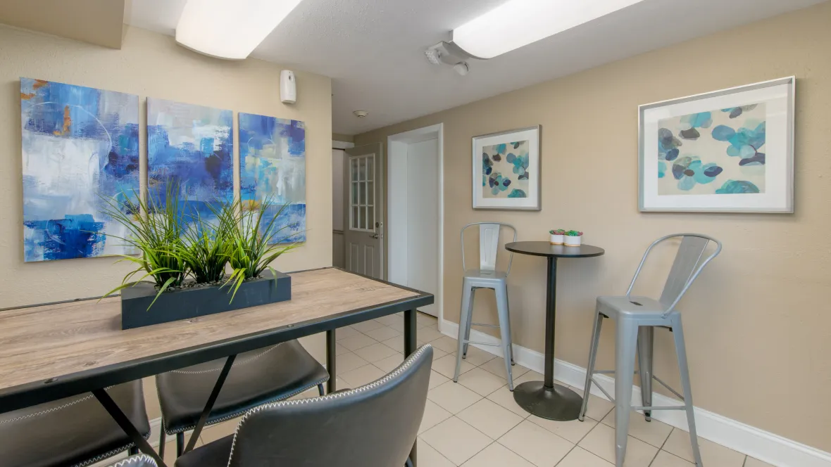 A well-lit, expansive room featuring a large table and chairs for work, alongside a bar-height table and stools.