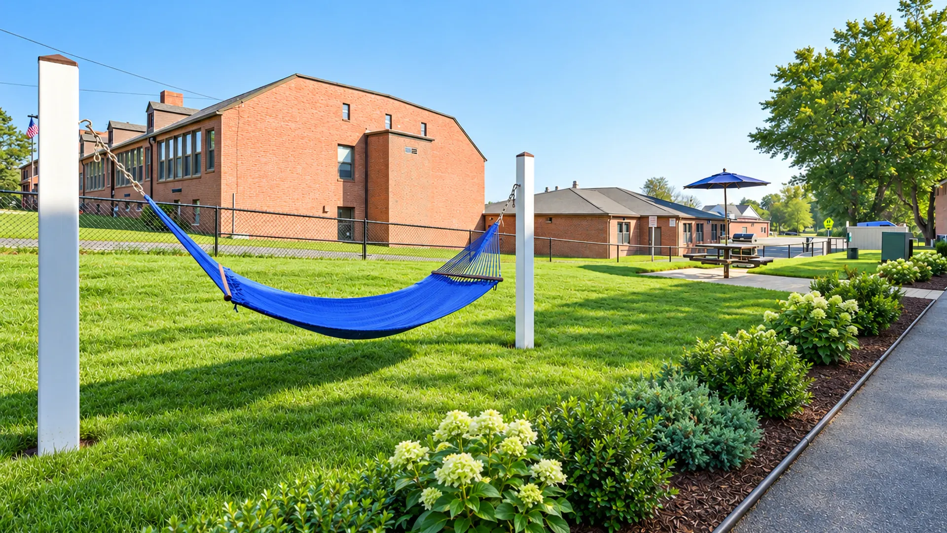 Blue hammock in a landscaped garden area at Country Manor Apartment Homes with manicured lawns, flower beds, and a nearby picnic area.