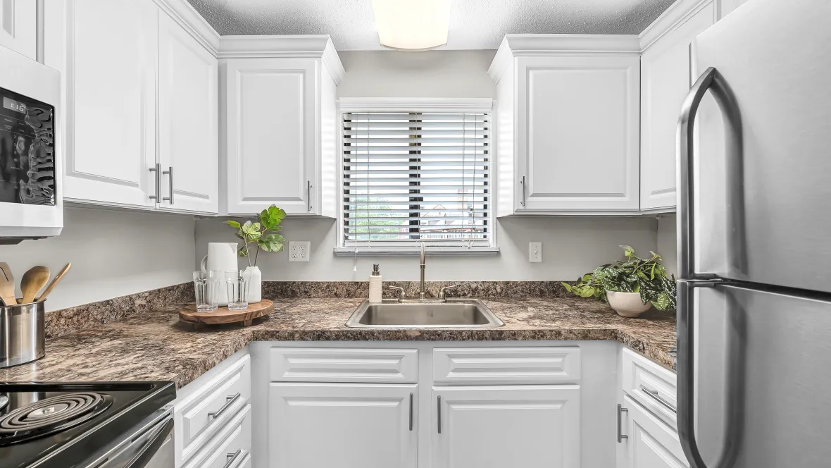 A modern kitchen in a u-shaped layout with white cabinetry and granite-style countertops.