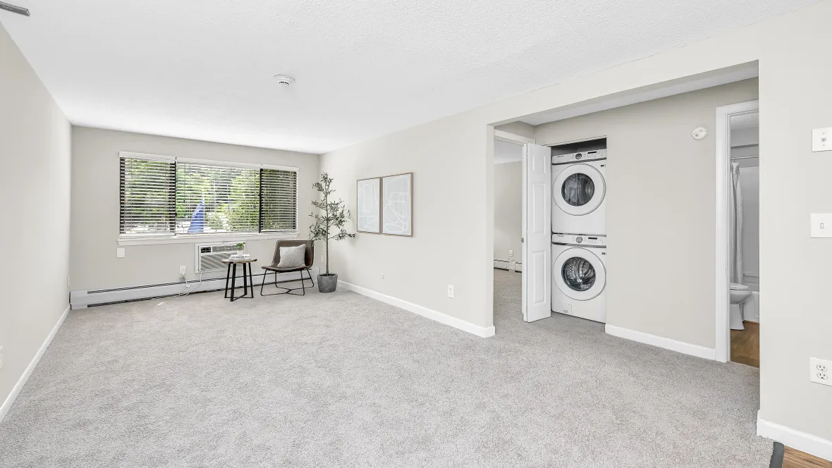 A welcoming living room with plush carpeting, flooded with natural light through large windows, creating a snug and inviting atmosphere.