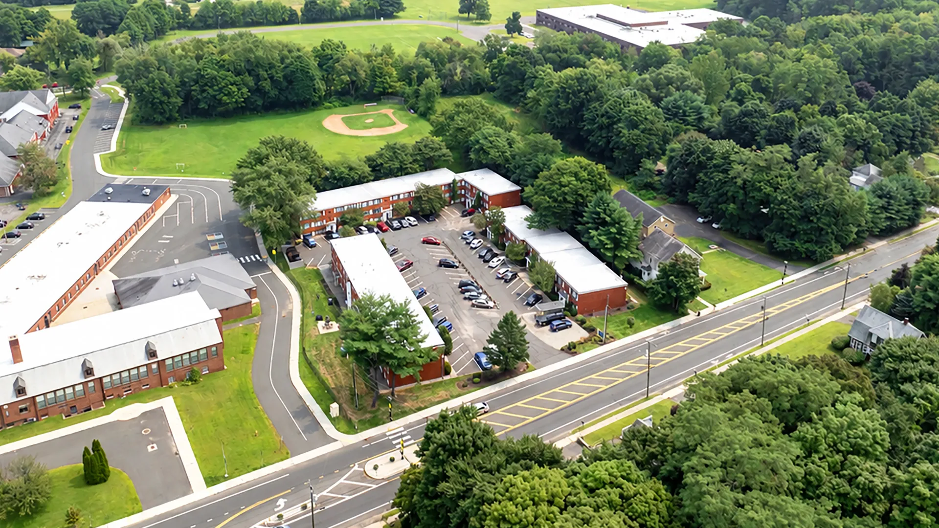 Aerial view of Country Manor Apartment Homes featuring residential buildings, parking areas, mature trees, and surrounding green space.