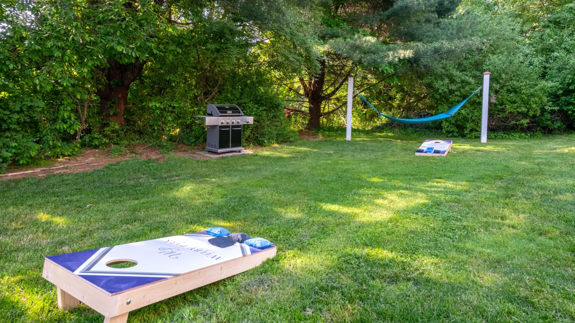 Cornhole game set up in an open grassy area with a BBQ grill and a hammock in the background at Welby Park Estates.